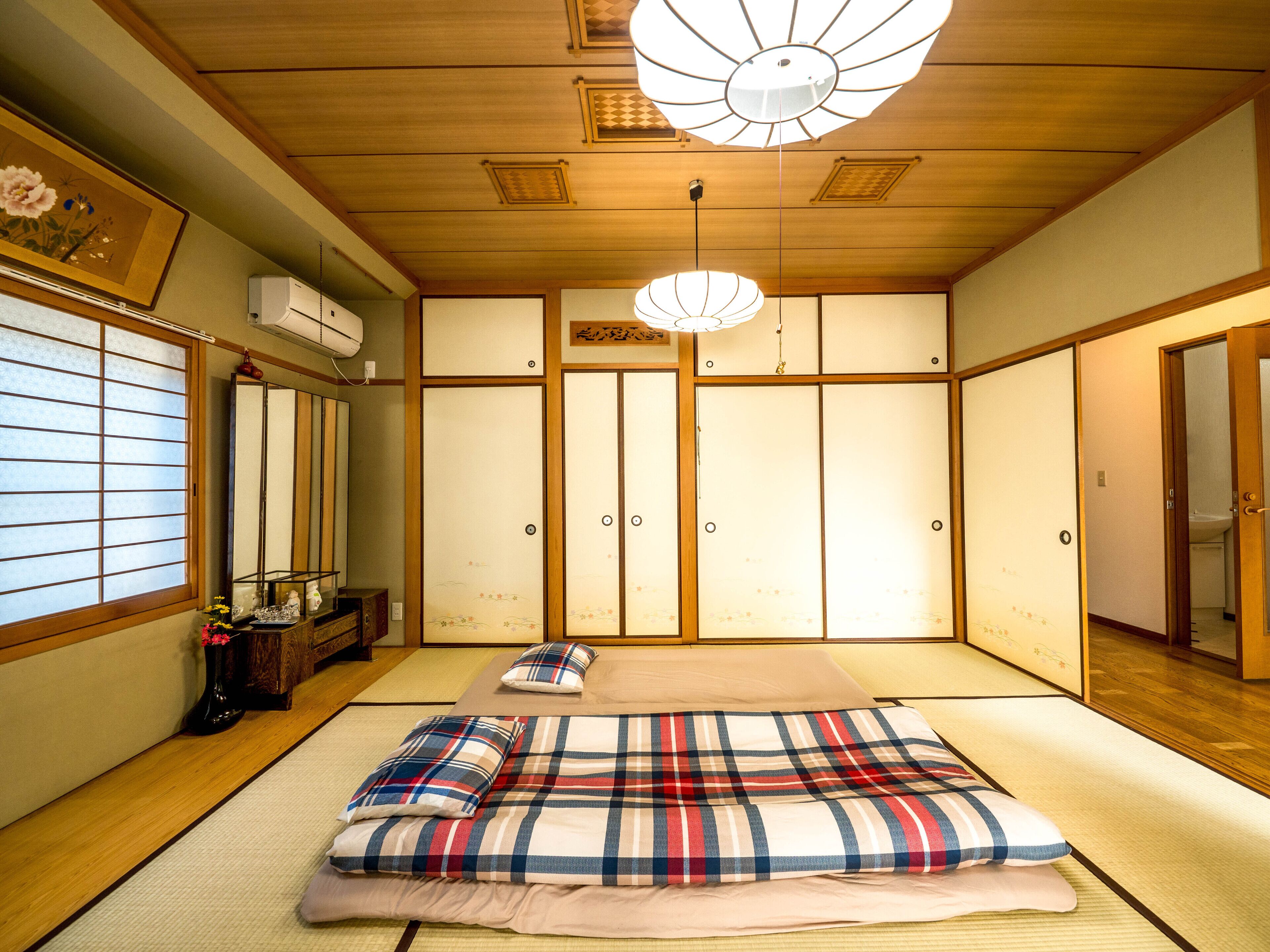 A traditional Japanese room with tatami flooring, a bed with a plaid bedspread, sliding shoji doors, and a hanging light fixture.