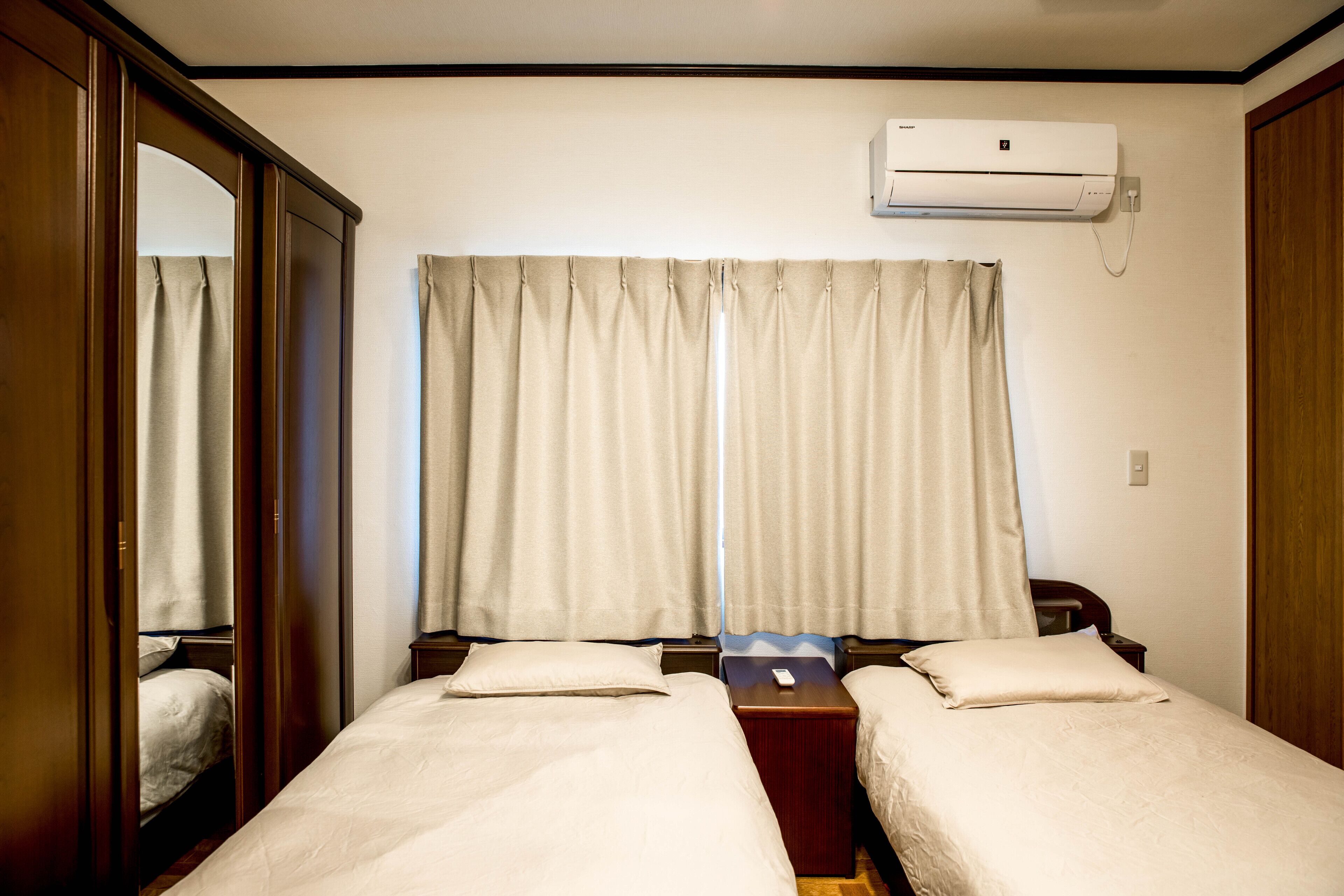 Habitación de hotel con dos camas, un armario de madera, una ventana con cortinas y un equipo de aire acondicionado.