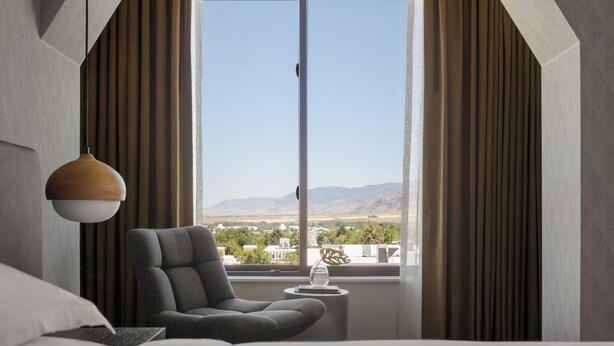 A modern hotel room with a large window, a grey armchair, a small side table, and a hanging pendant light. - Kimpton Armory Hotel Bozeman by IHG (Bozeman)