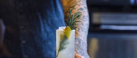 Drinkki, jossa on koriste, ja jonka kädessään pitää tatuoitu henkilö, baaritiskillä.