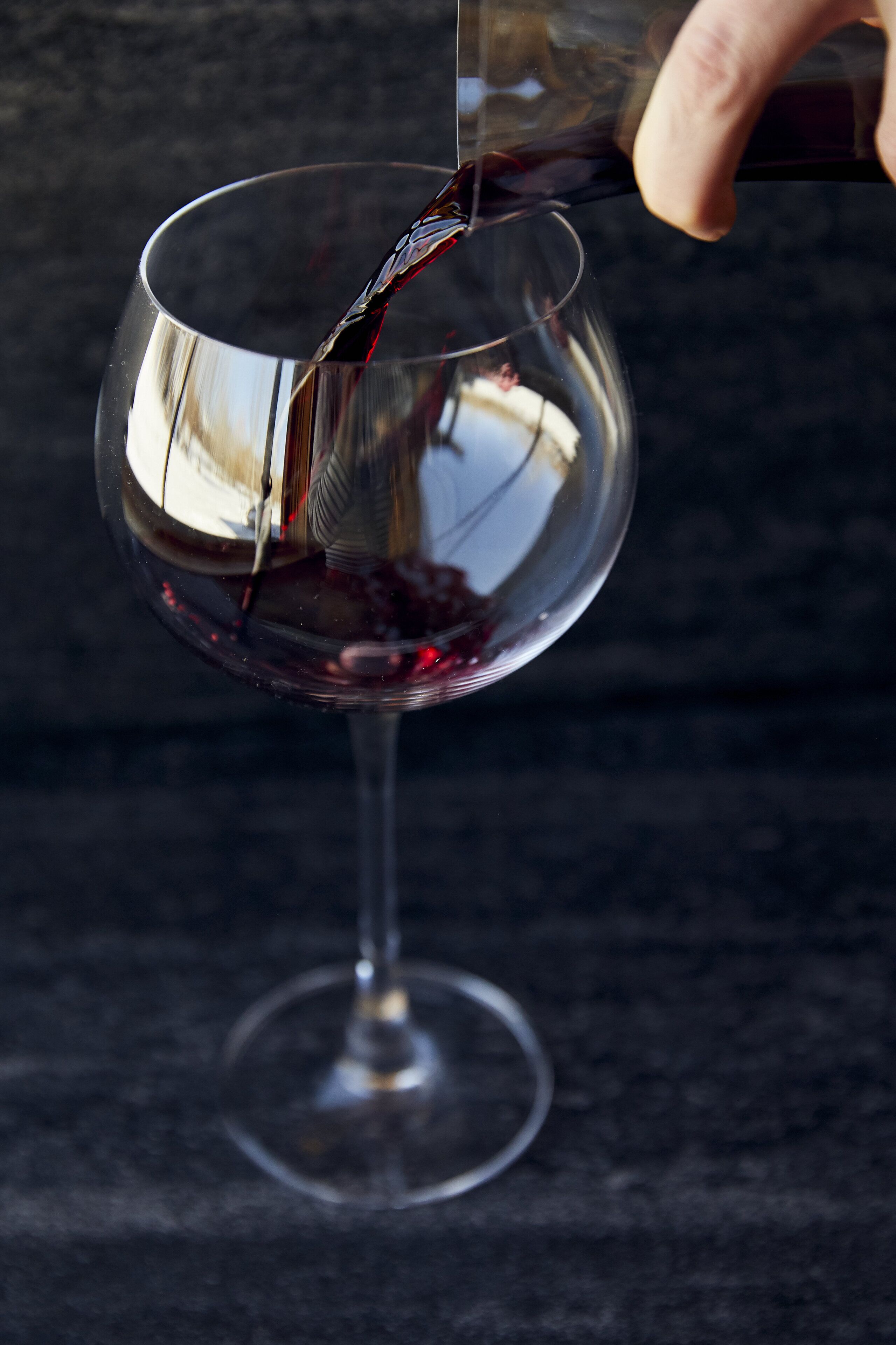 A hand pouring red wine into a clear glass.