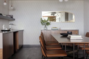A modern dining area with a wooden table, leather chairs, a mirror, and a vase with greenery. - Kimpton Armory Hotel Bozeman by IHG (Bozeman)