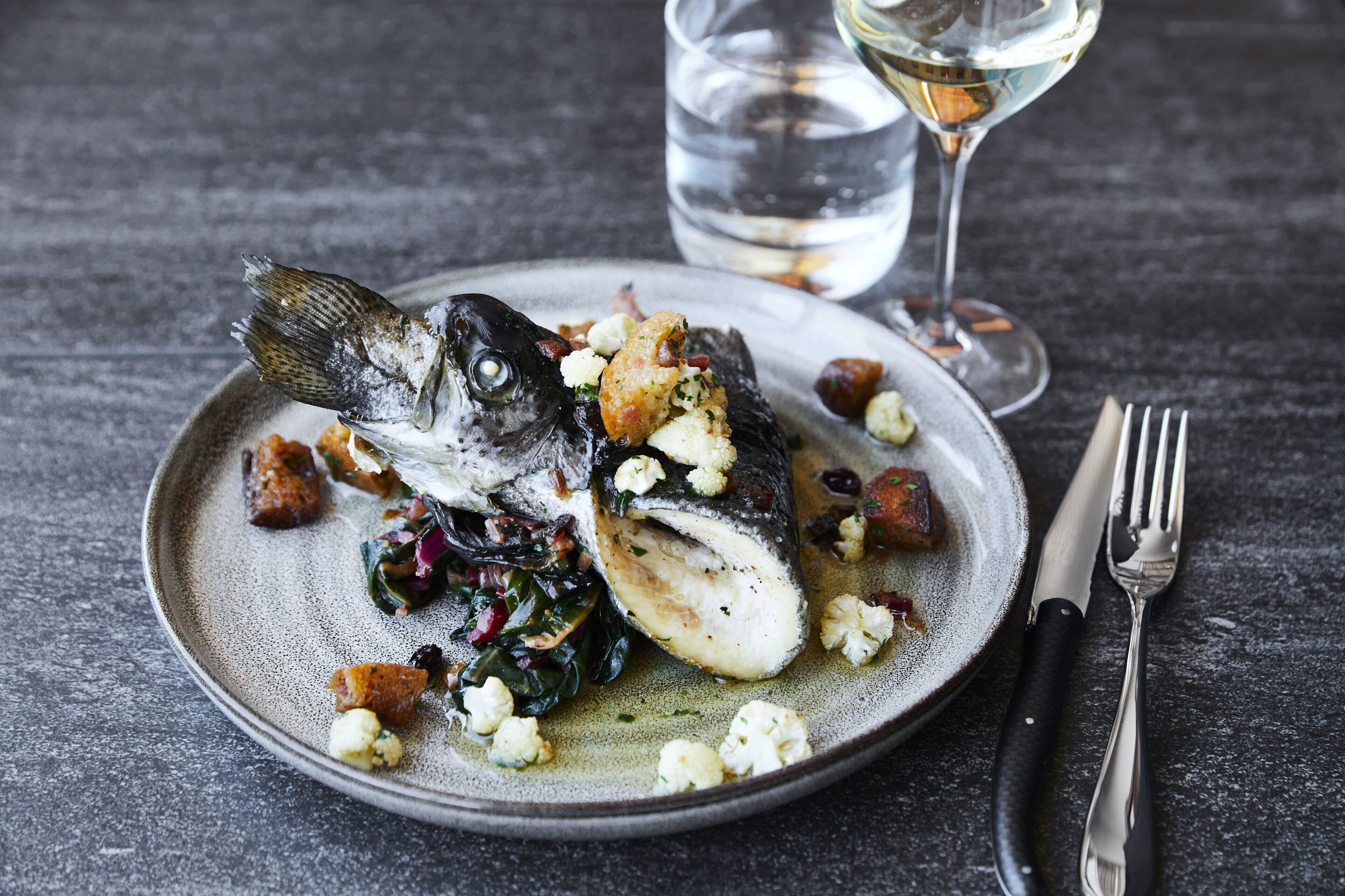 A plate of fish with vegetables and croutons.