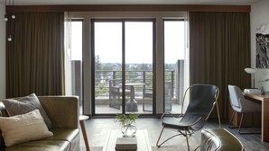 A modern living room with a sofa, a chair, a small table with a plant, and a view of a balcony with outdoor furniture. - Kimpton Armory Hotel Bozeman by IHG (Bozeman)