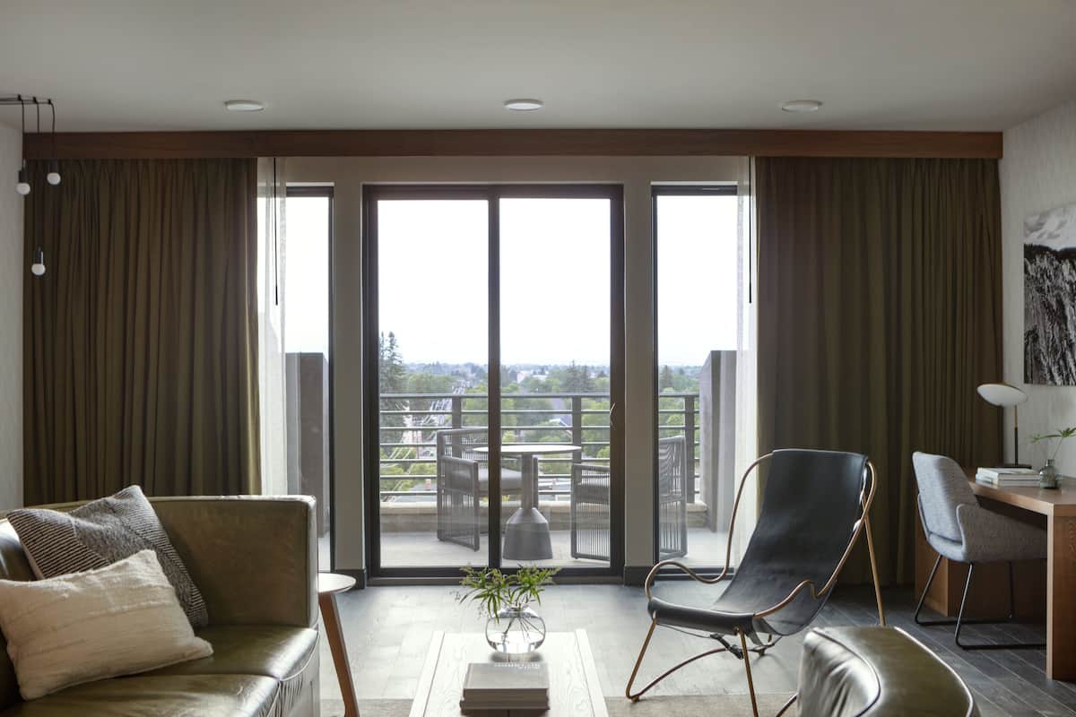 A modern living room with a sofa, a chair, a small table with a plant, and a view of a balcony with outdoor furniture.