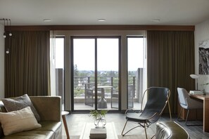 Una sala de estar moderna con un sofá, una butaca, una mesita con una planta y vistas a un balcón con mobiliario exterior.