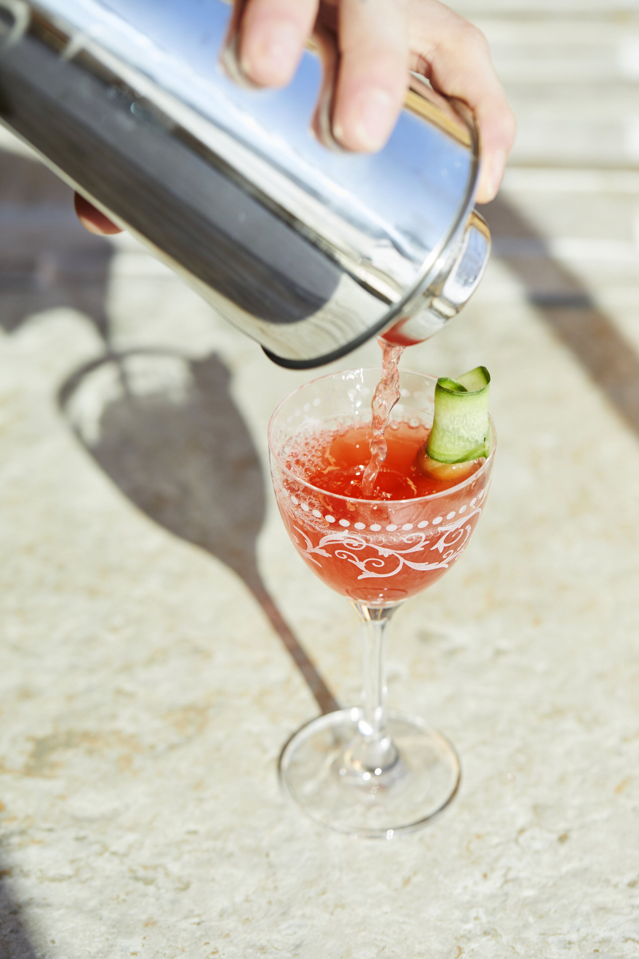 Eine Hand gießt ein Getränk in ein Glas, verziert mit einer Gurke.