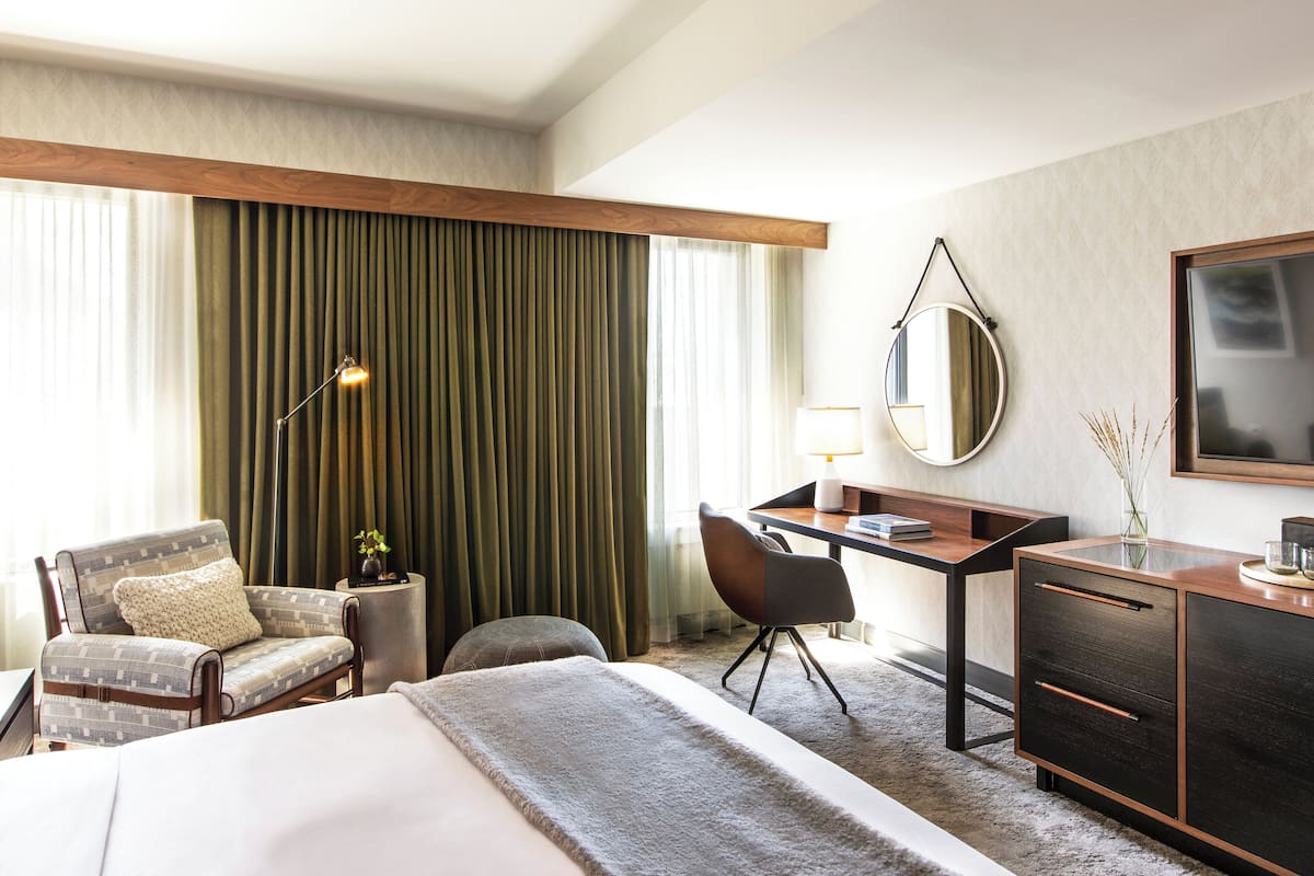A hotel room with a bed, a desk, a chair, a lamp, a mirror, and a dresser.