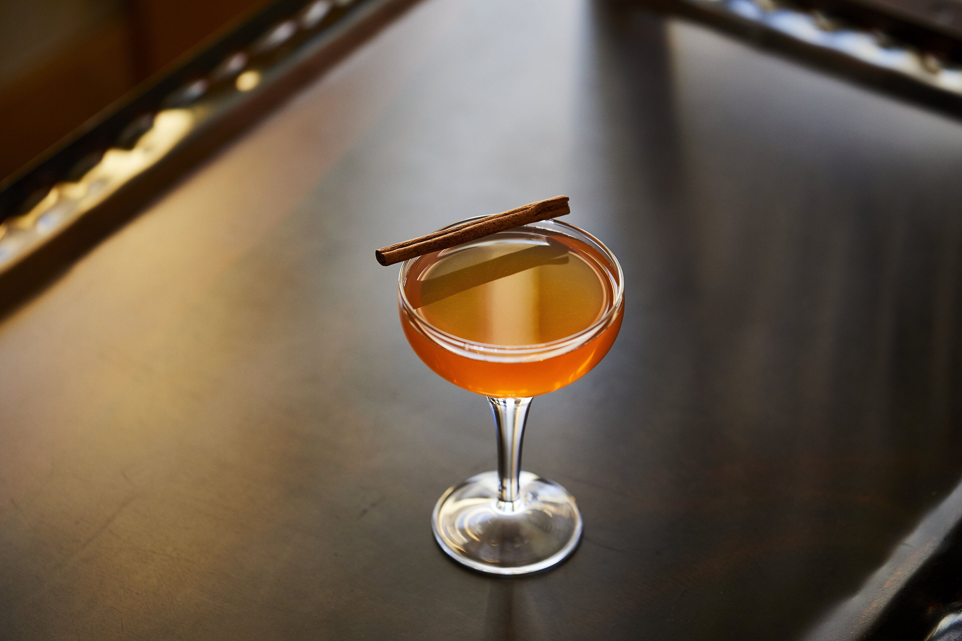 Un verre à cocktail avec une tige de cannelle posée sur une surface réfléchissante.