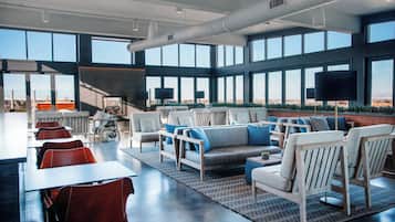 A modern lounge area with seating and tables, large windows offering a view, and a staircase leading to an upper level.
