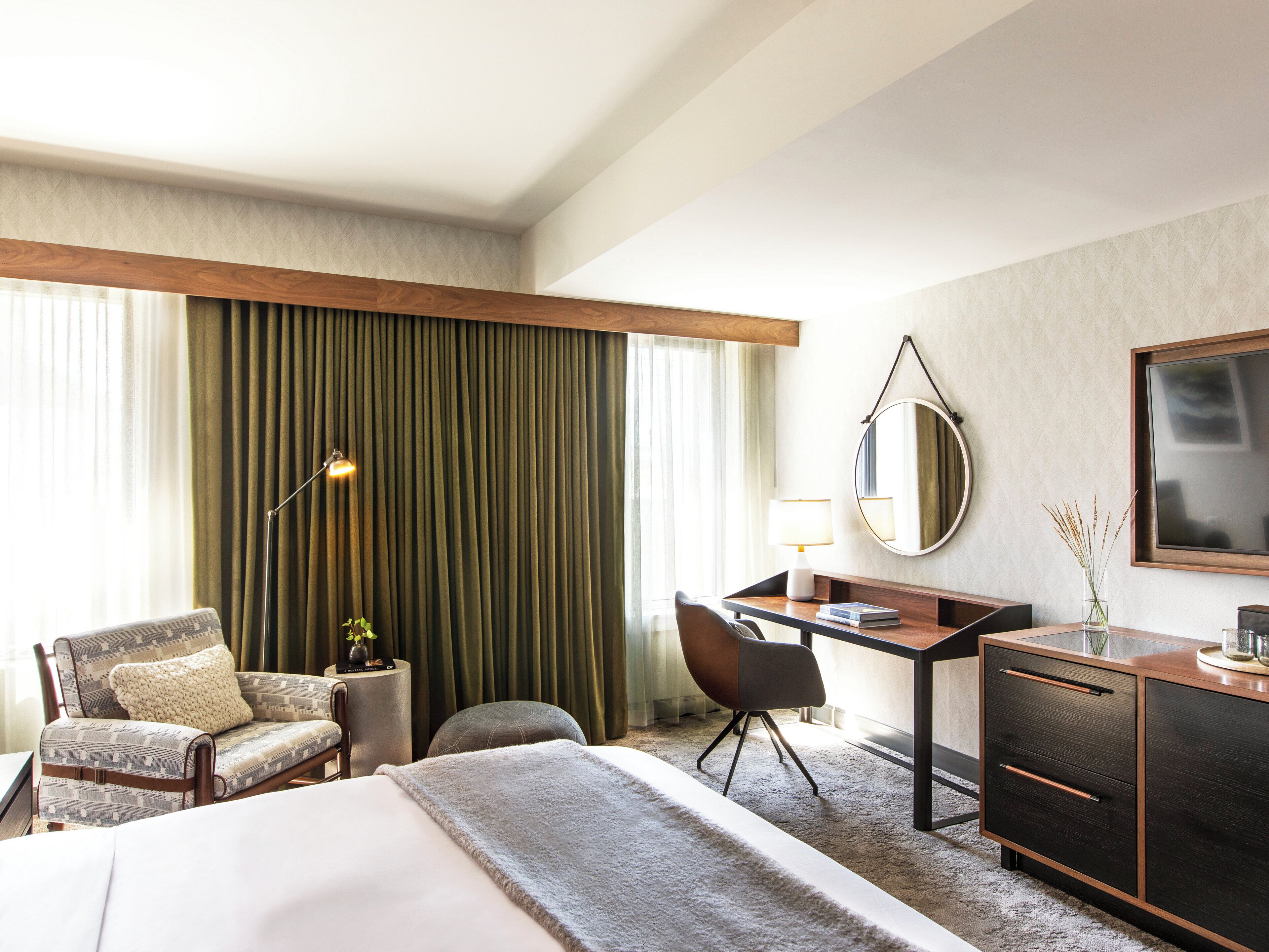 Una habitación de hotel con una cama, un escritorio, una silla, una lámpara, un espejo y un aparador.
