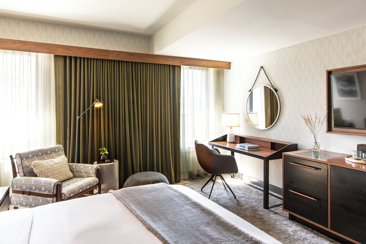 Una habitación de hotel con una cama, un escritorio, una silla, una lámpara, un espejo y un aparador.