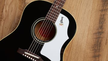 A close-up of a guitar with a white pickguard and a black body, featuring the Gibson logo.