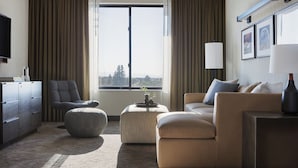 A modern hotel room with a large window, a sofa, a chair, a small ottoman, and a television on a cabinet. - Kimpton Armory Hotel Bozeman by IHG (Bozeman)