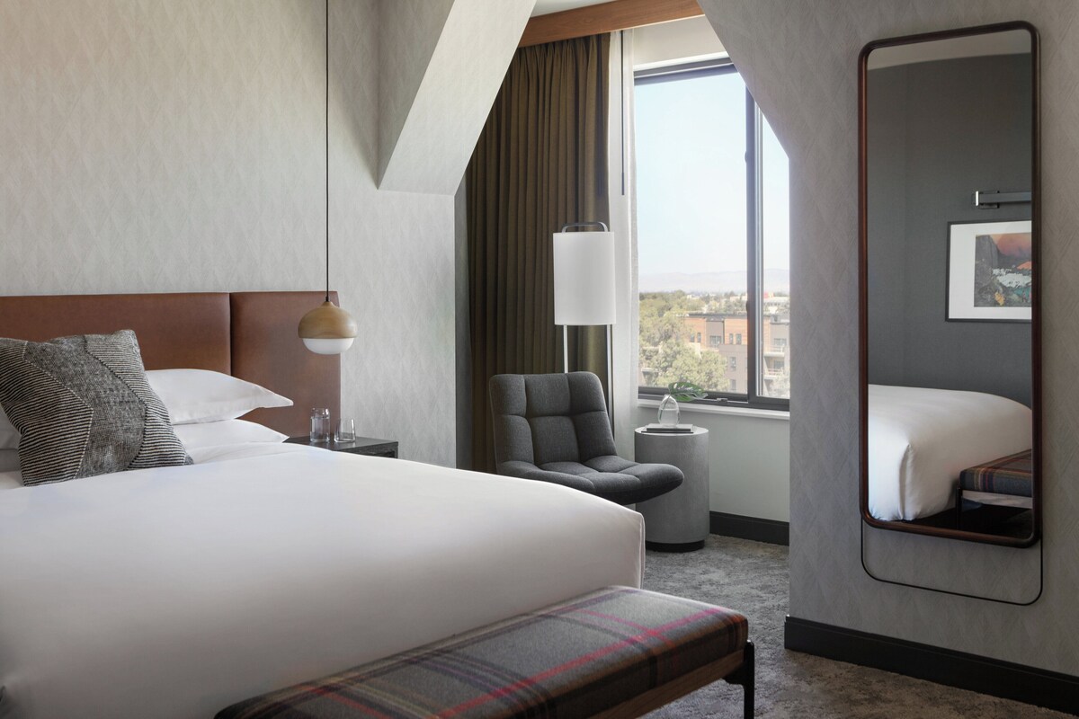 Een moderne hotelkamer met een groot bed, een stoel, een bijzettafeltje en een grote spiegel.