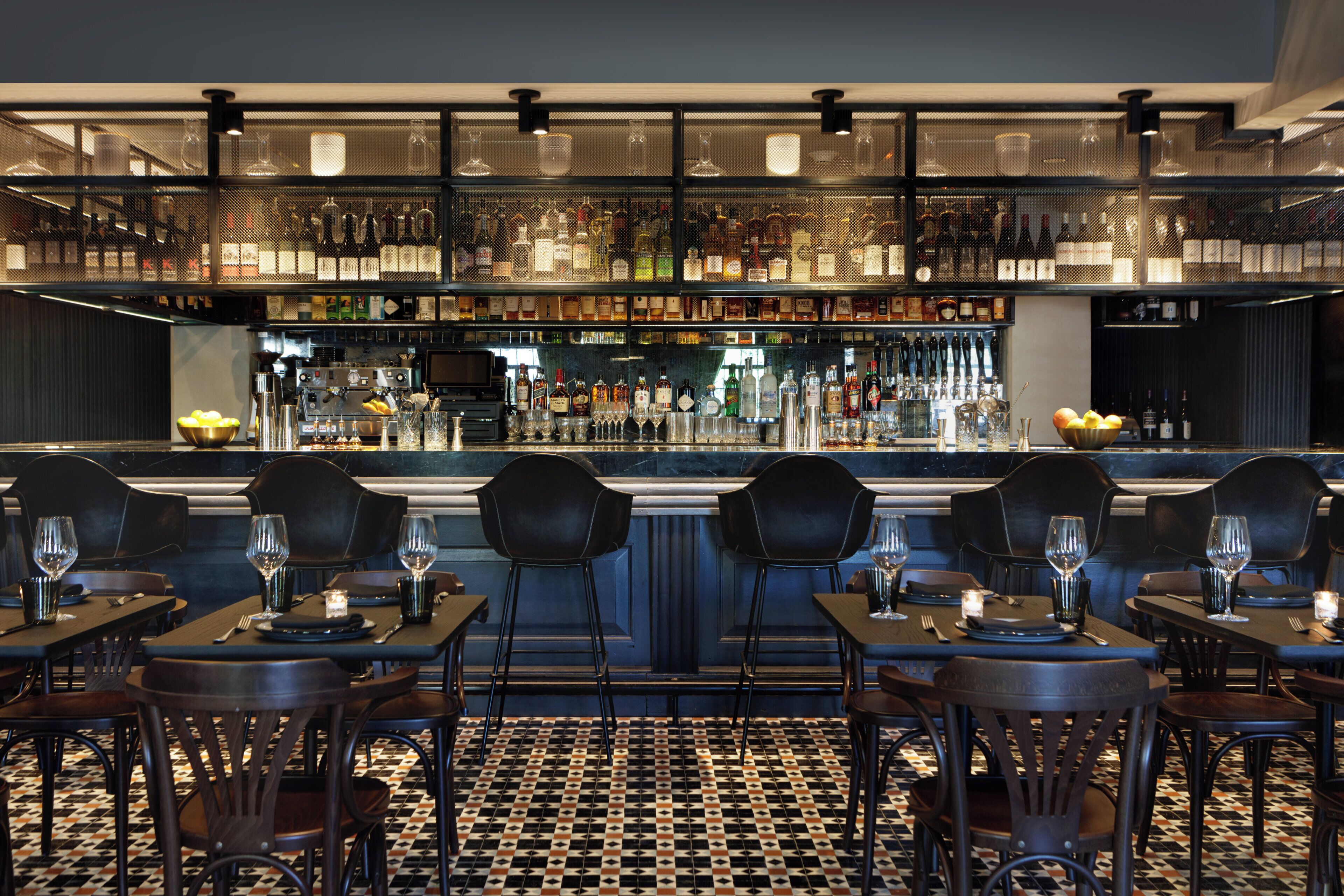A bar area with multiple seating arrangements and a variety of bottles on shelves.