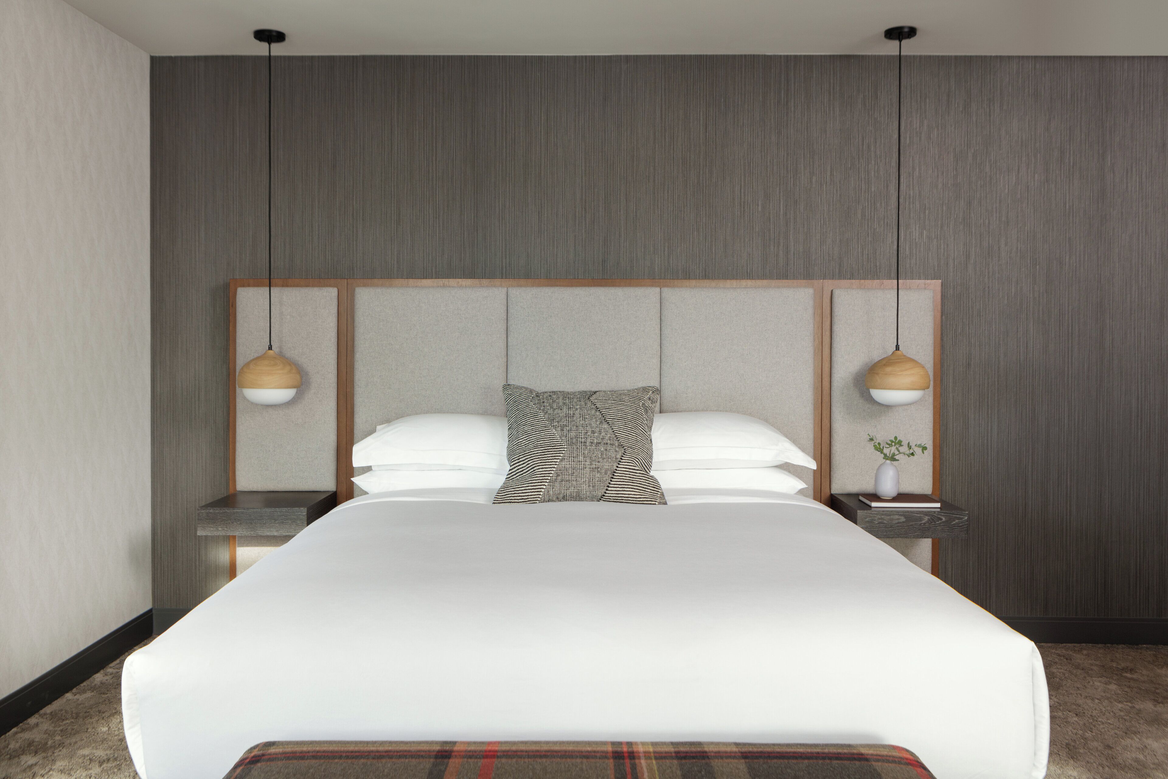 Una habitaci ón de hotel moderna con una cama grande, dos mesitas de noche y una pequeña planta en maceta.