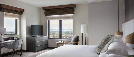 Hotelkamer met een groot bed, een bureau met stoel, een televisie en uitzicht op de stad door de ramen.