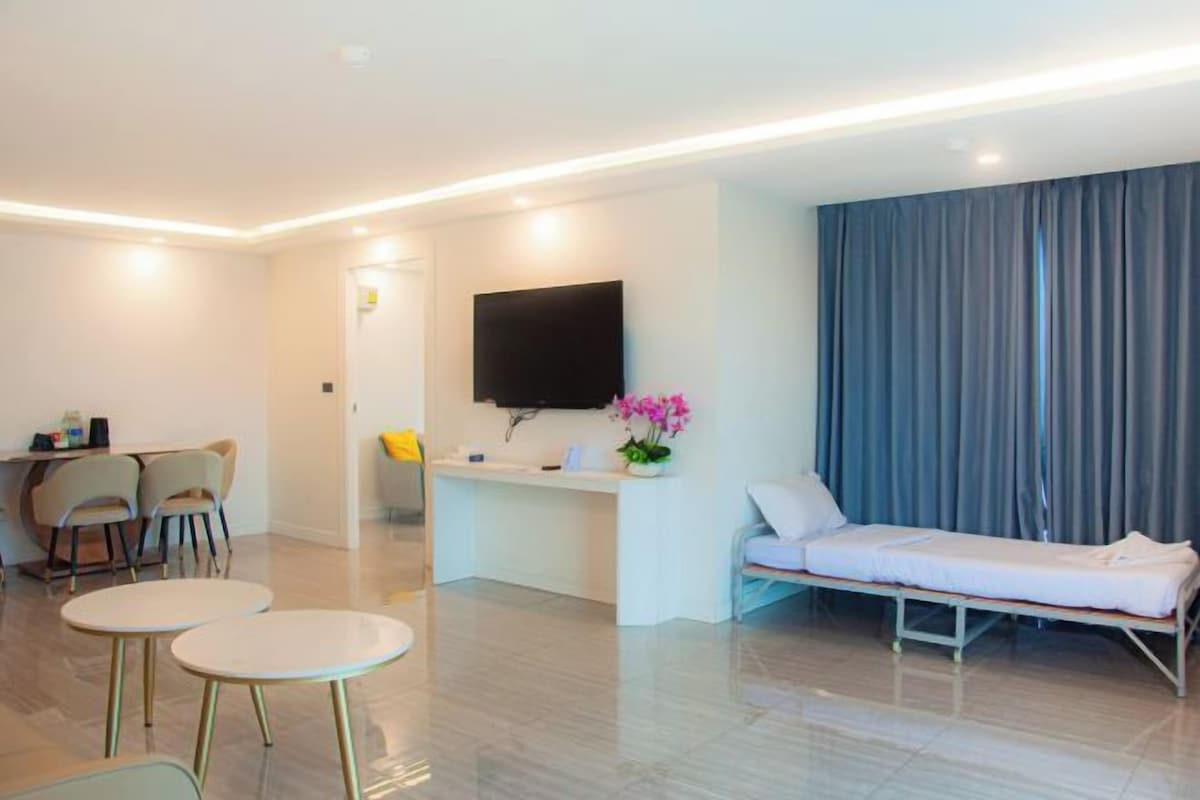 A modern hotel room with a flat-screen TV, a small desk, a bedside table, a chair, and a bed.
