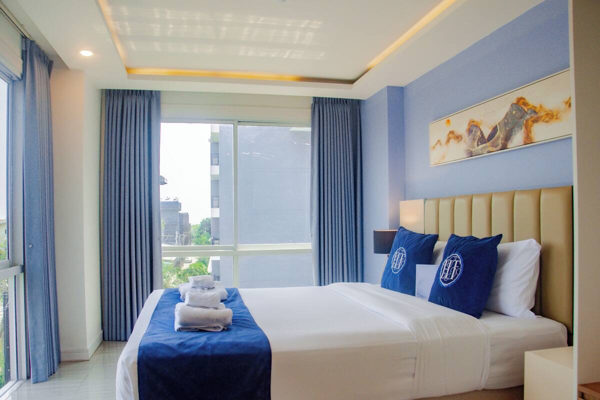 A hotel room with a large bed, a city view, and a painting on the wall.