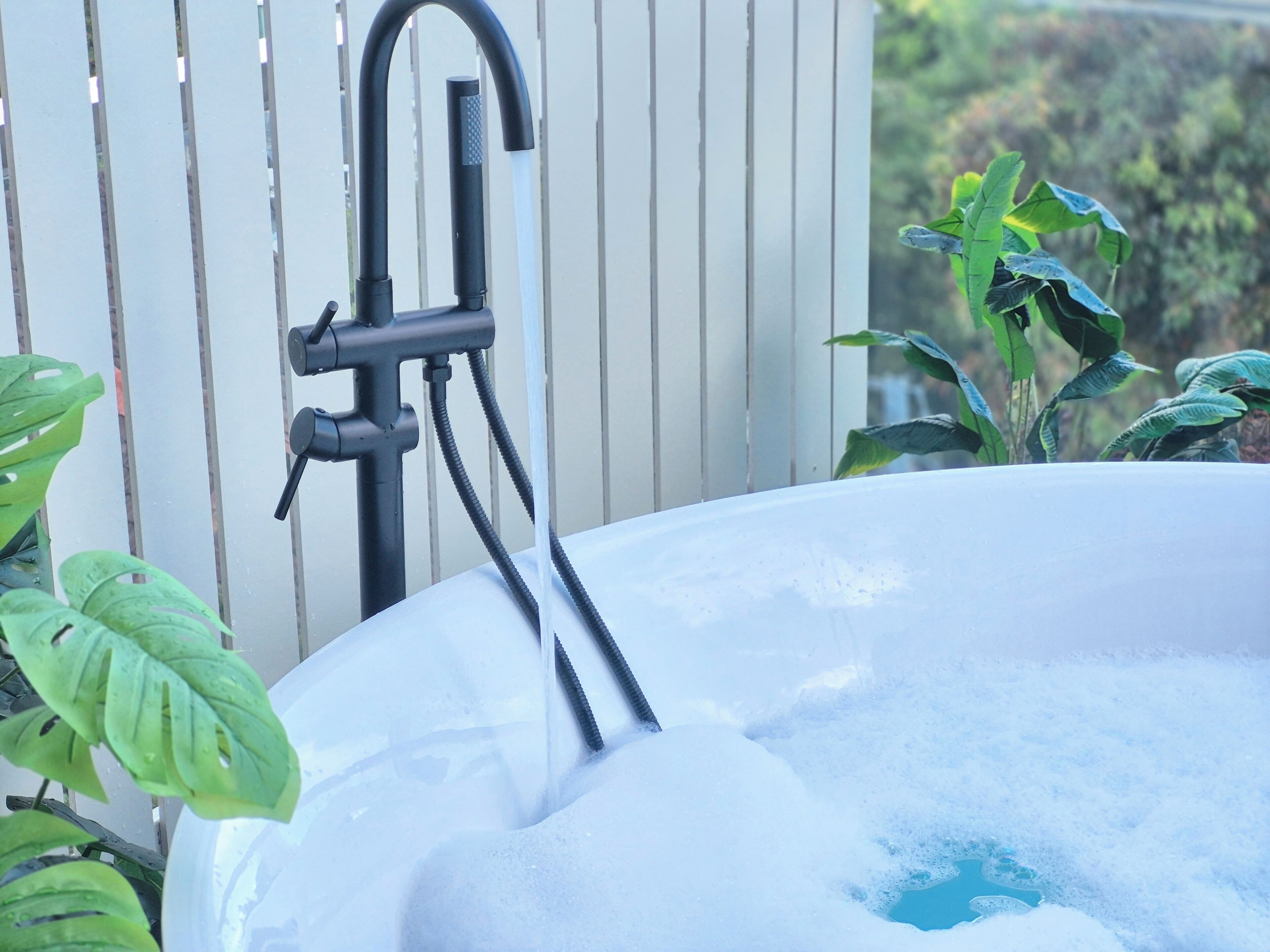 A hot tub with a black faucet and a hose, surrounded by green plants.
