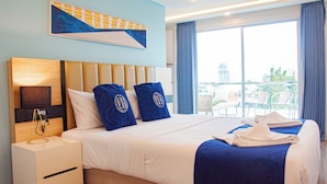 Ein Hotelzimmer mit einem großen Bett, einem Nachttisch, einem Wandbild und einem Balkon mit Sitzgelegenheiten.