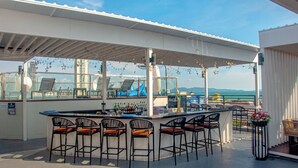 Eine Dachterrasse mit Blick auf die Stadtlandschaft, ausgestattet mit einer Bar, mehreren Barhocker und Außenmöbeln.