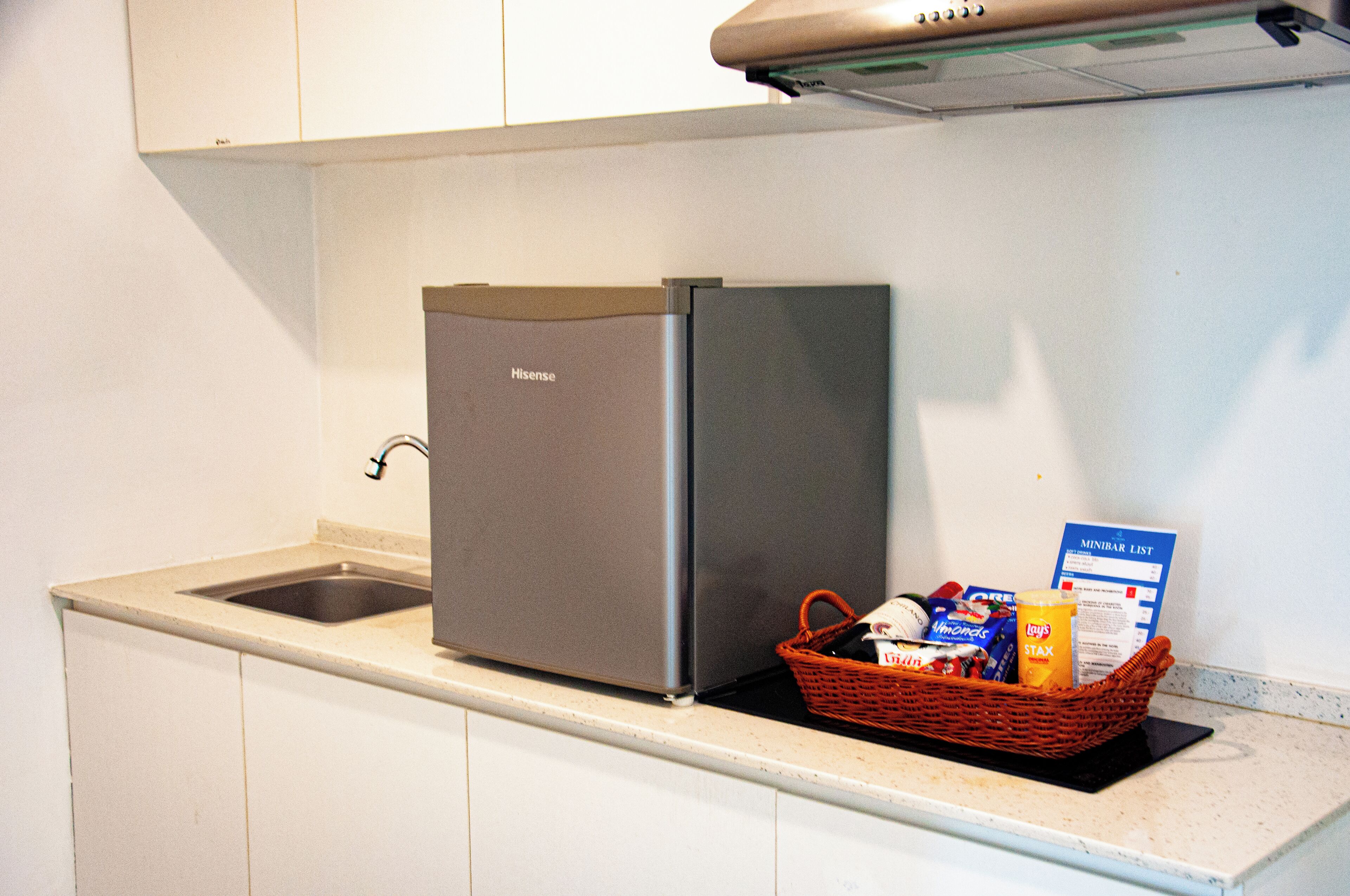 A compact kitchen with a built-in refrigerator, a sink, and a basket containing groceries.