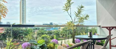 A balcony with a round table and two chairs, surrounded by lush greenery and flowers.