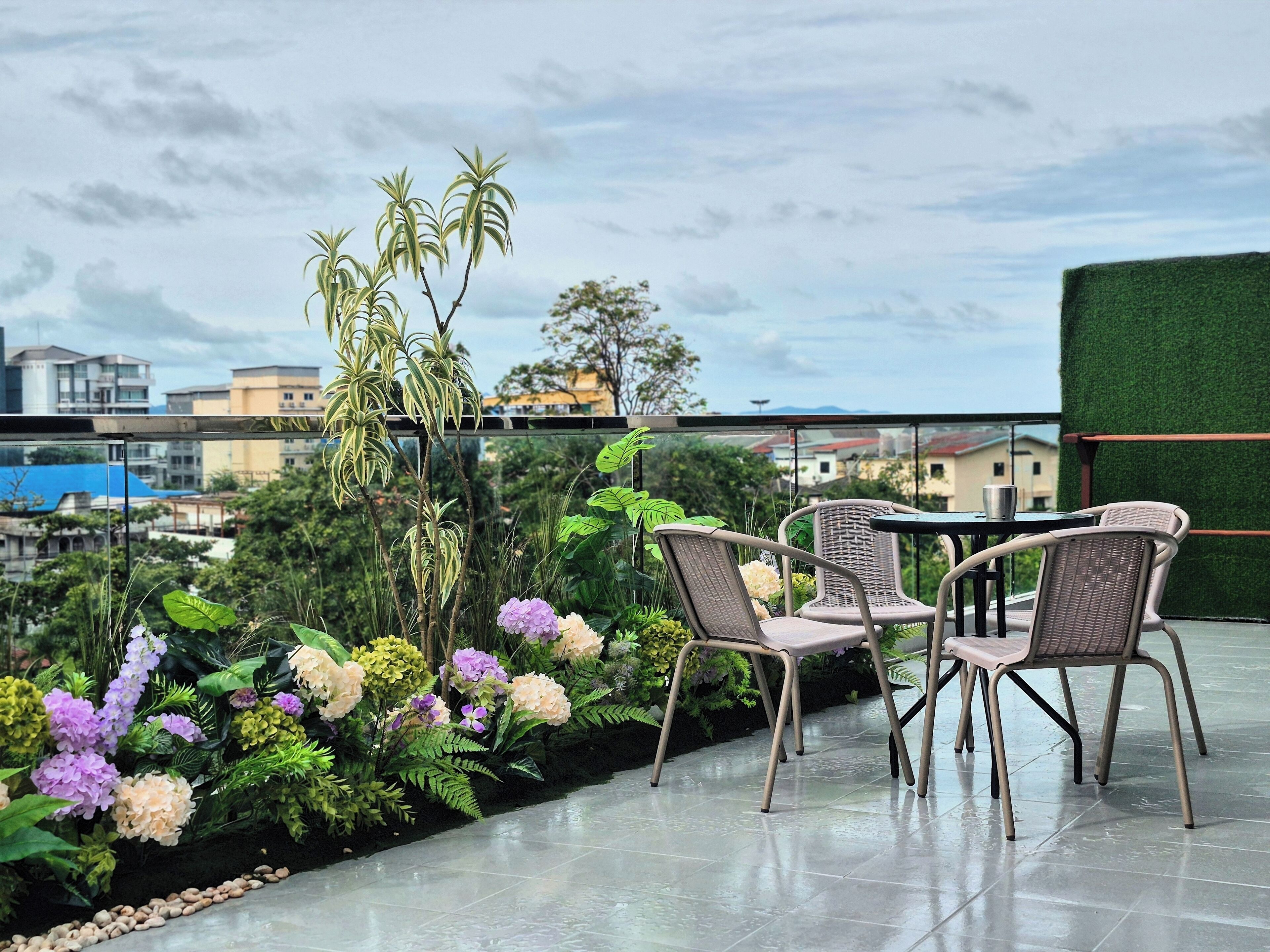 A terrace with wicker chairs, a table, and a variety of flowers.