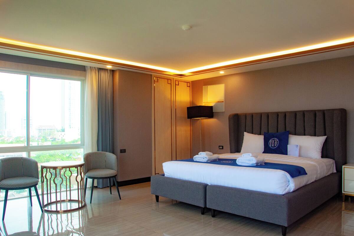 A hotel room with a large bed, two armchairs, a small table, and a view of the city through the window.