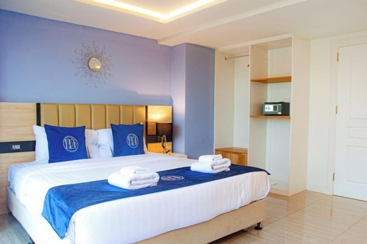 Habitación de hotel con cama, mesita de noche, televisor montado en la pared y puerta que da a otra habitación.