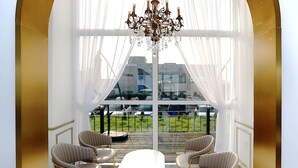 A modern room with a large window, a chandelier, and four chairs around a table.