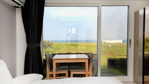 A bedroom with a large bed, a wooden table with two chairs, and a sliding glass door leading to a balcony with a view of the sea and a boat.