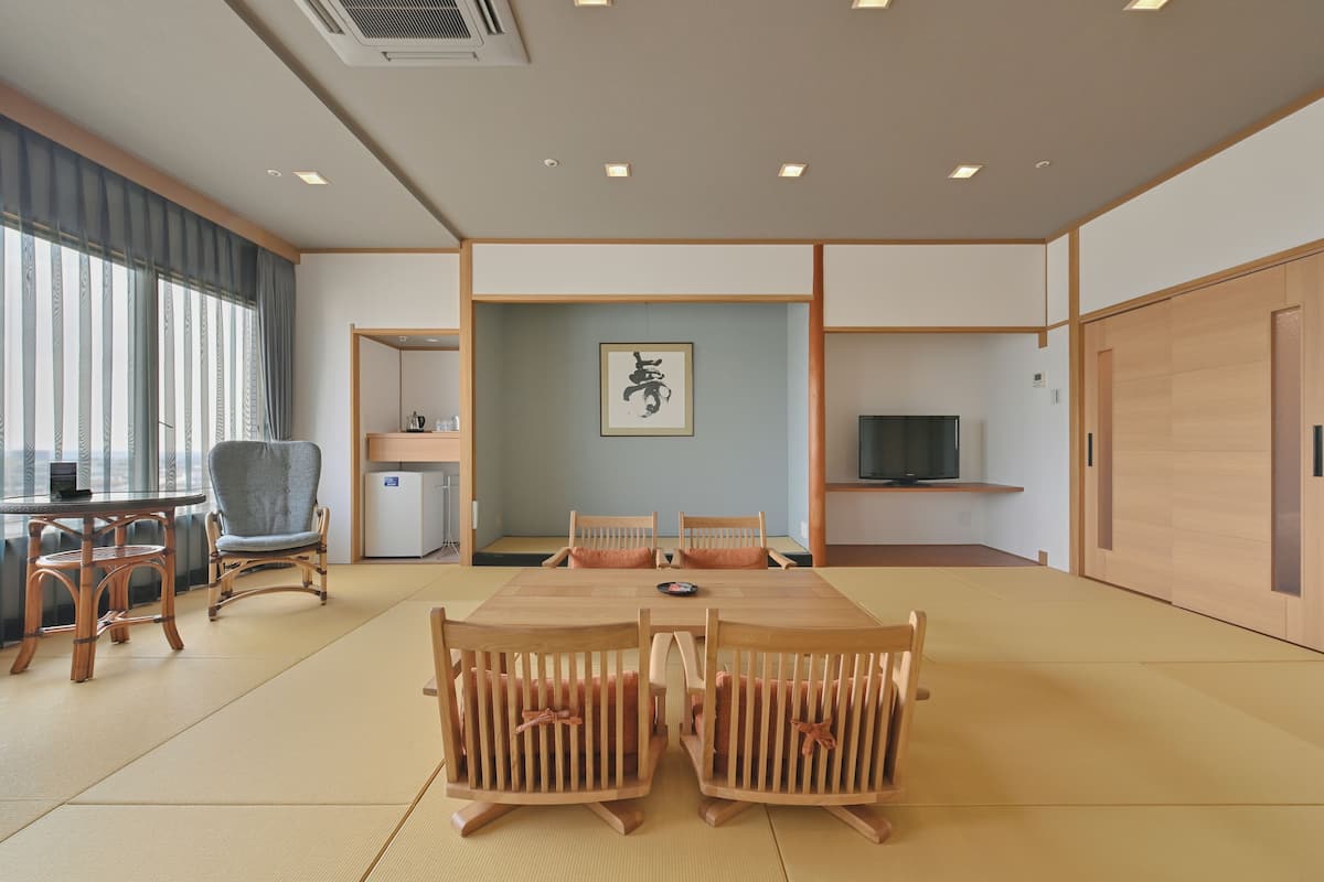 Een traditionele Japanse kamer met tatami vloer, een lage tafel met houten stoelen, een televisie en een schuifdeur.