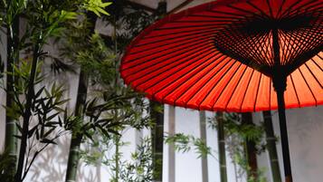 A red parasol with a lattice design, surrounded by tall bamboo plants.