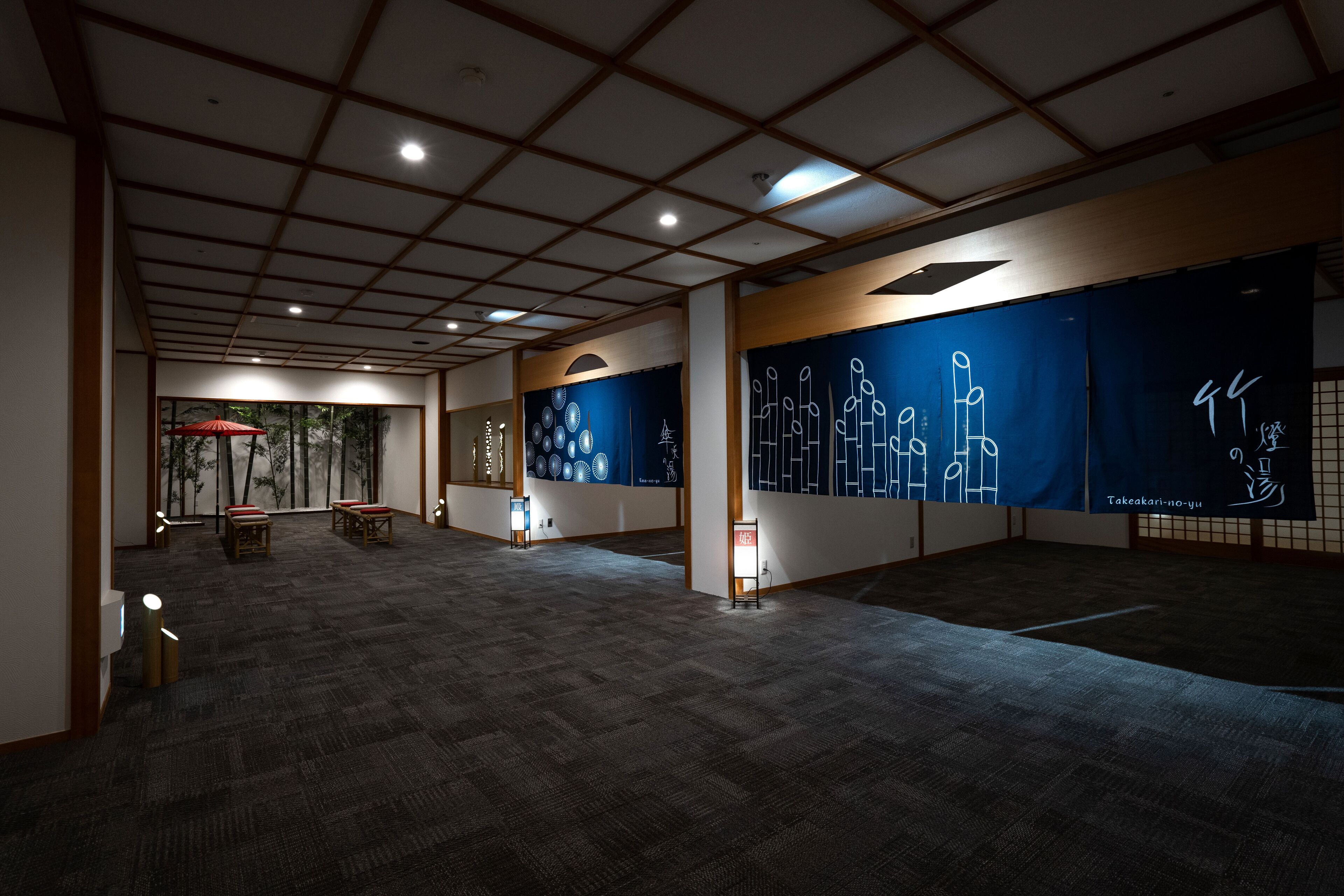 A spacious room with a high ceiling, traditional tatami mat flooring, and large windows with a view of trees.