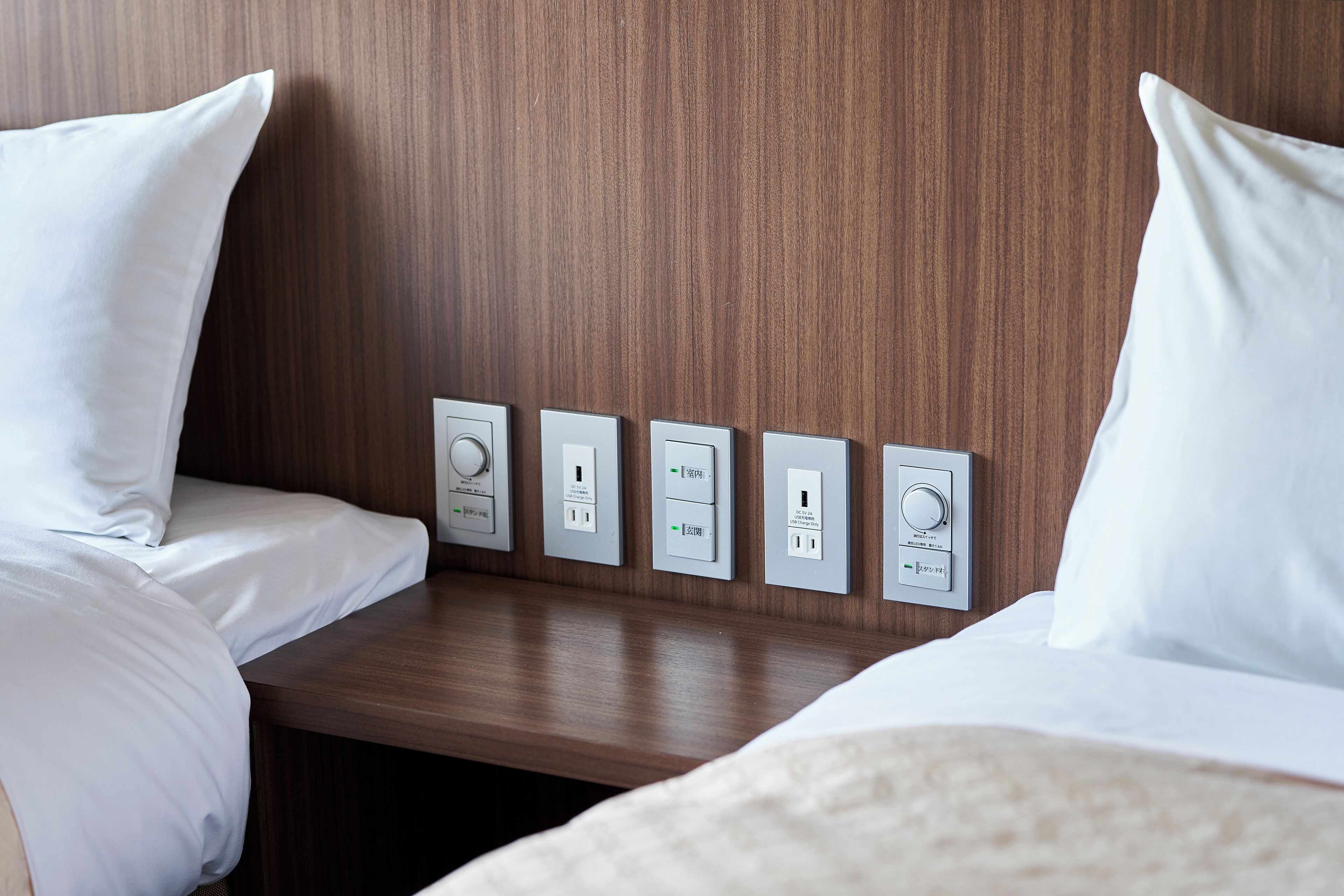 A hotel room with a wooden headboard, a bedside table, and four electrical outlets.
