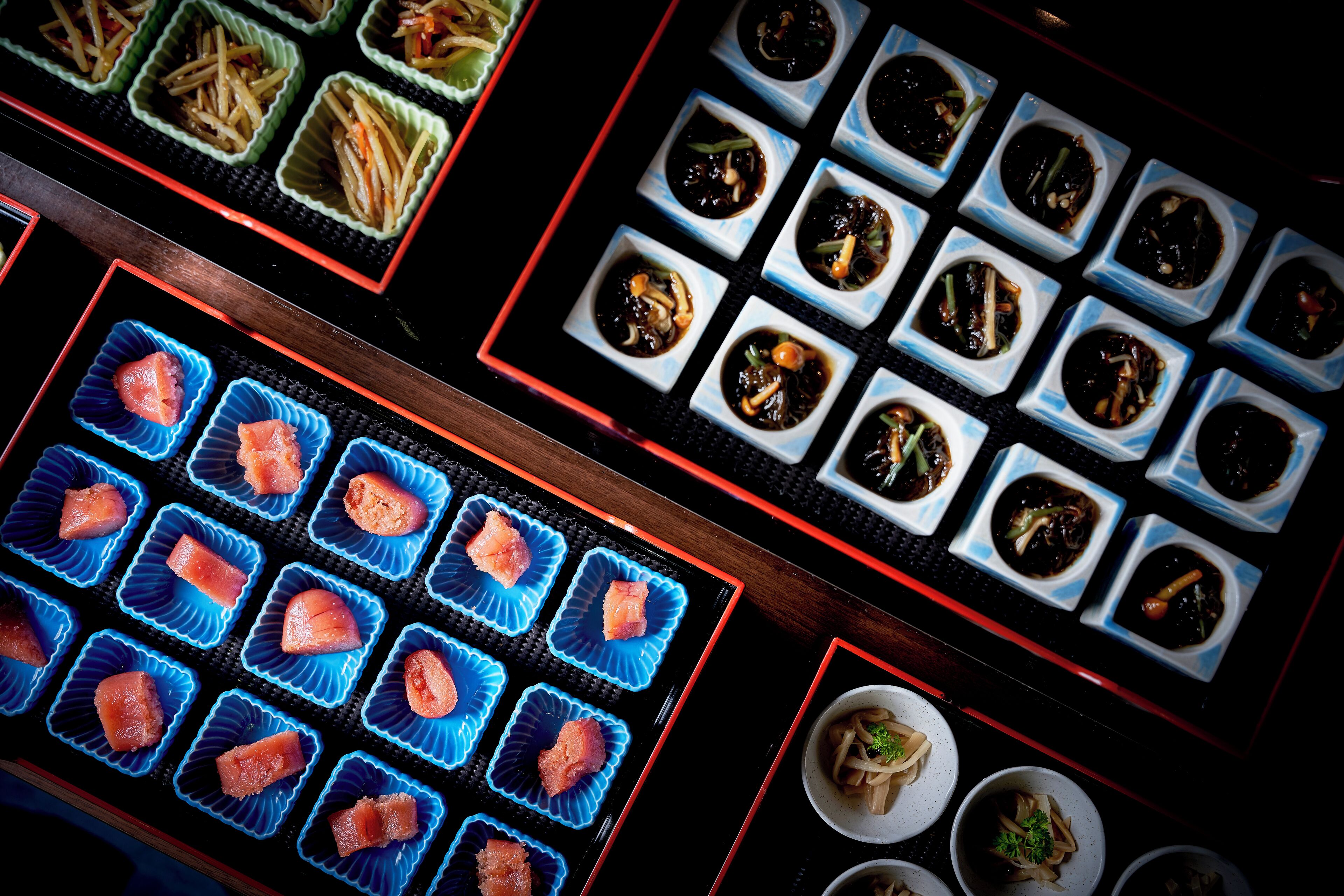 A variety of dishes arranged in square and rectangular containers, likely part of a buffet or food service.