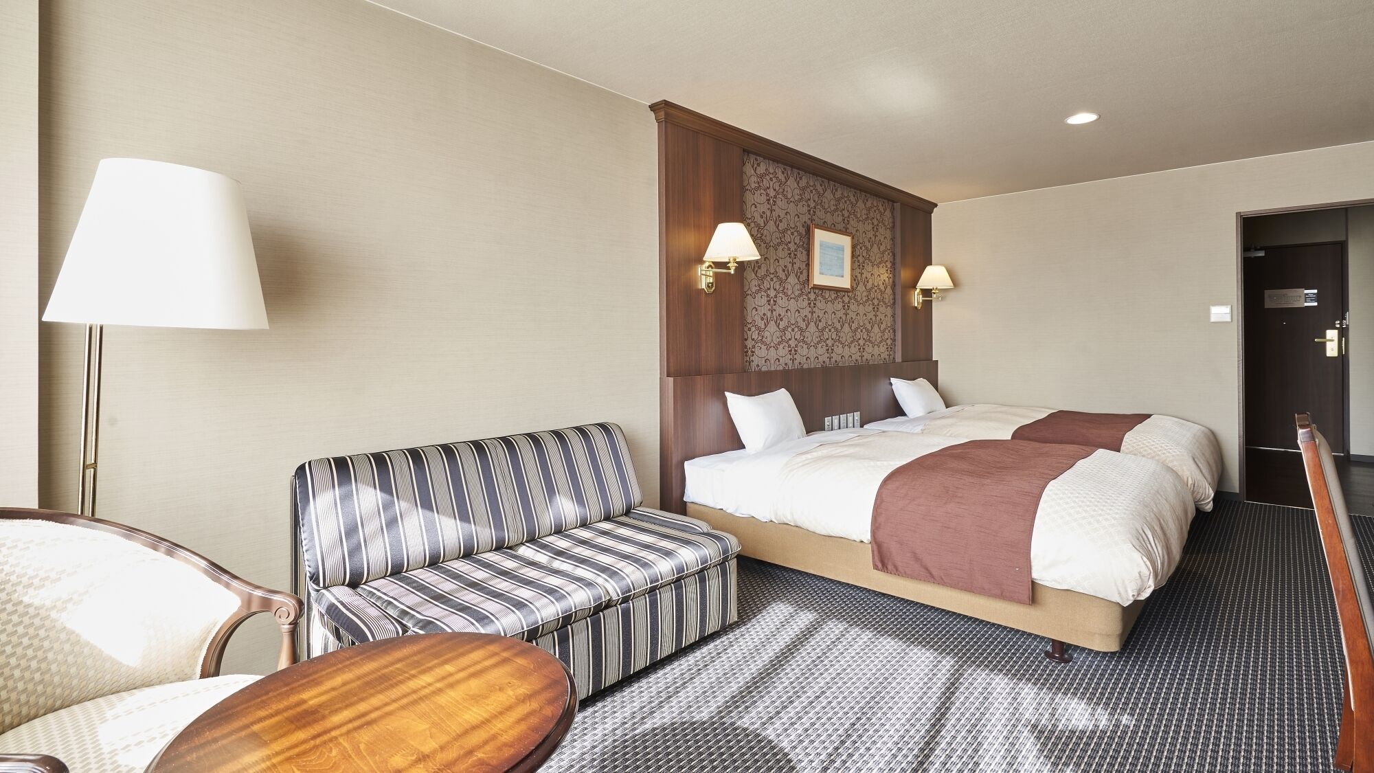 Une chambre d’hôtel avec un lit, un canapé à rayures, une table en bois et une lampe.