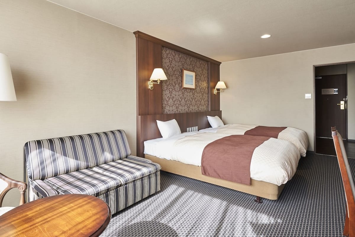Een hotelkamer met een bed, een gestreept bankje, een houten tafel en een lamp.
