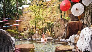 A clear outdoor pool with rocks and trees, surrounded by umbrellas.