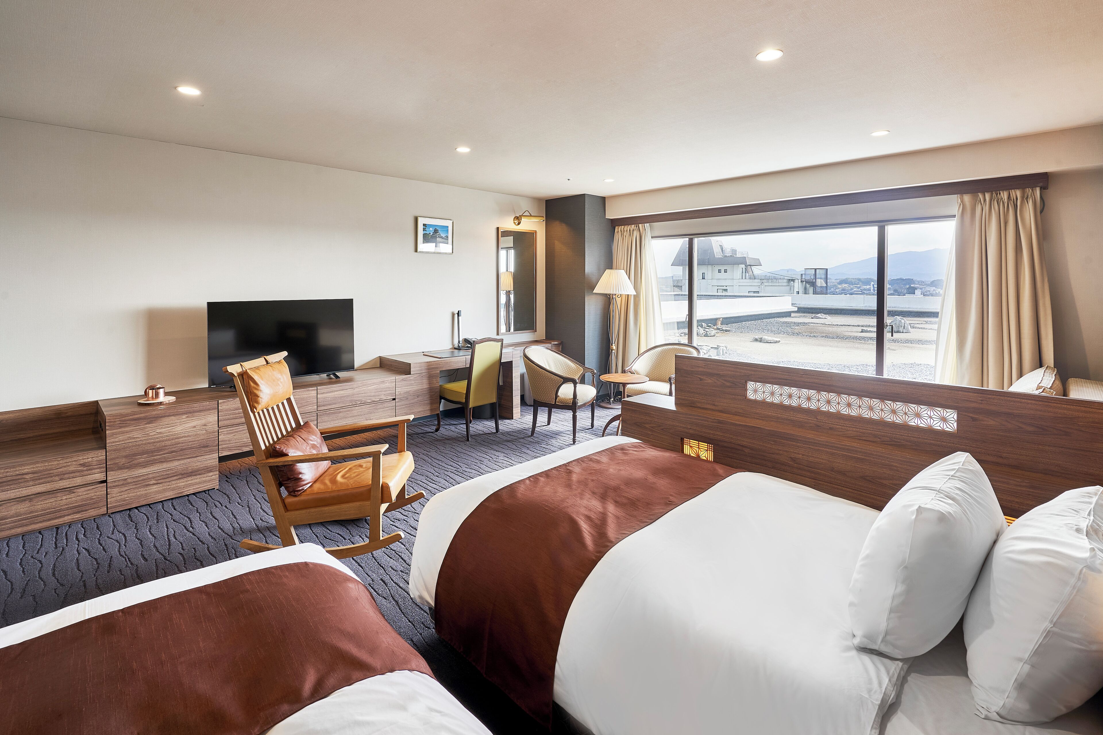 Habitación de hotel con una cama grande, un escritorio, una silla, un televisor y vistas de la ciudad.