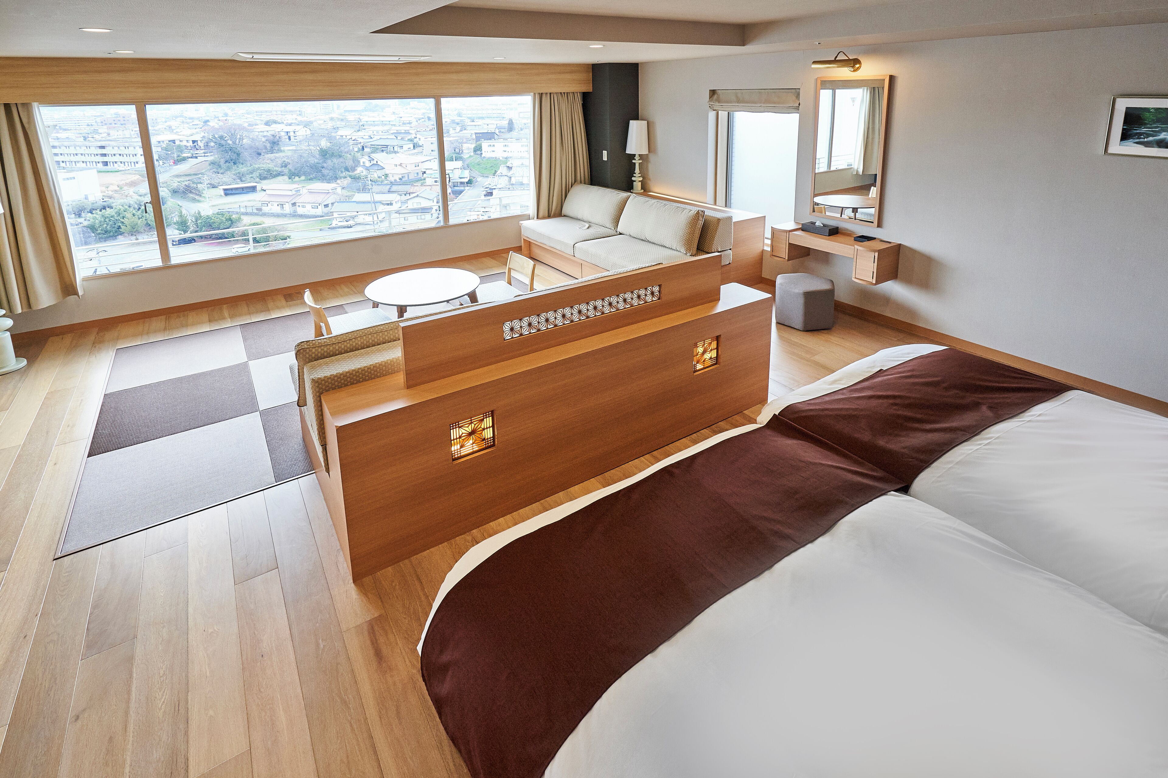 A hotel room with a large bed, a sofa, a desk, and a view of the city.