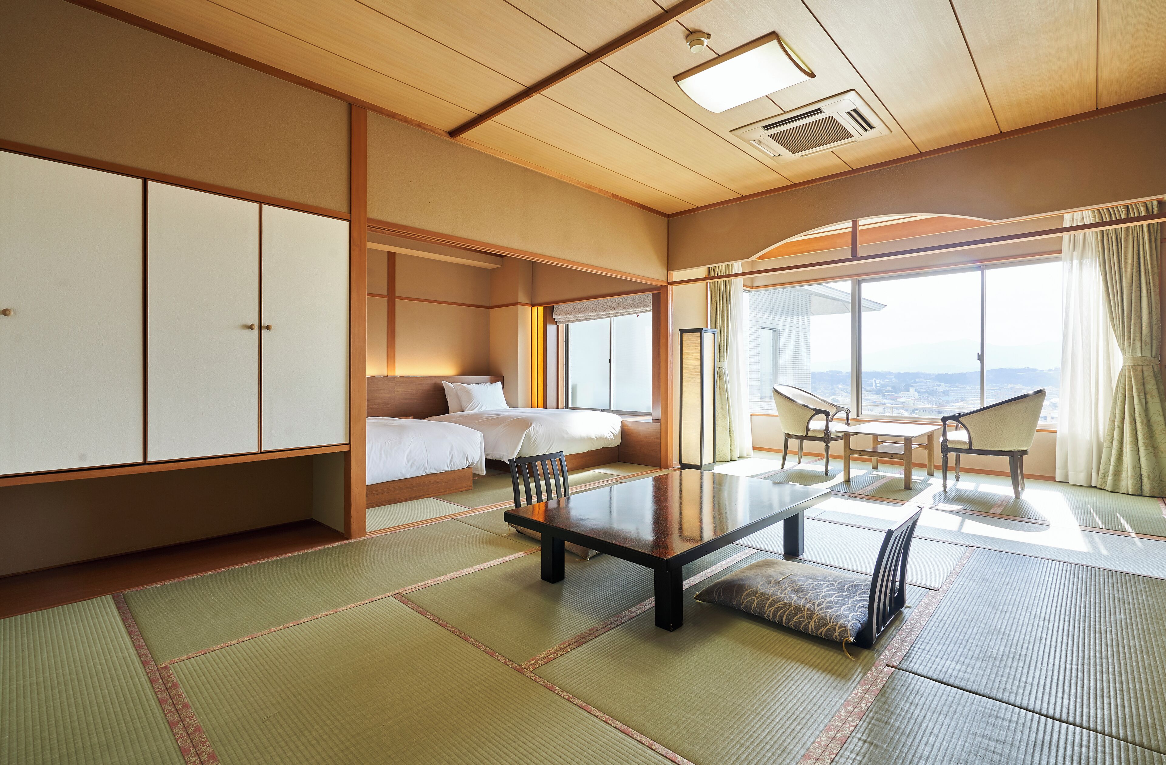 A traditional Japanese-style room with tatami flooring, a low table, and a bed with white bedding.
