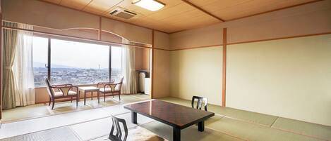 Ein Raum mit Tatami-Matten, einem niedrigen Tisch, Stühlen, großen Fenstern mit Blick auf die Stadt und einer Holzbodenverkleidung.