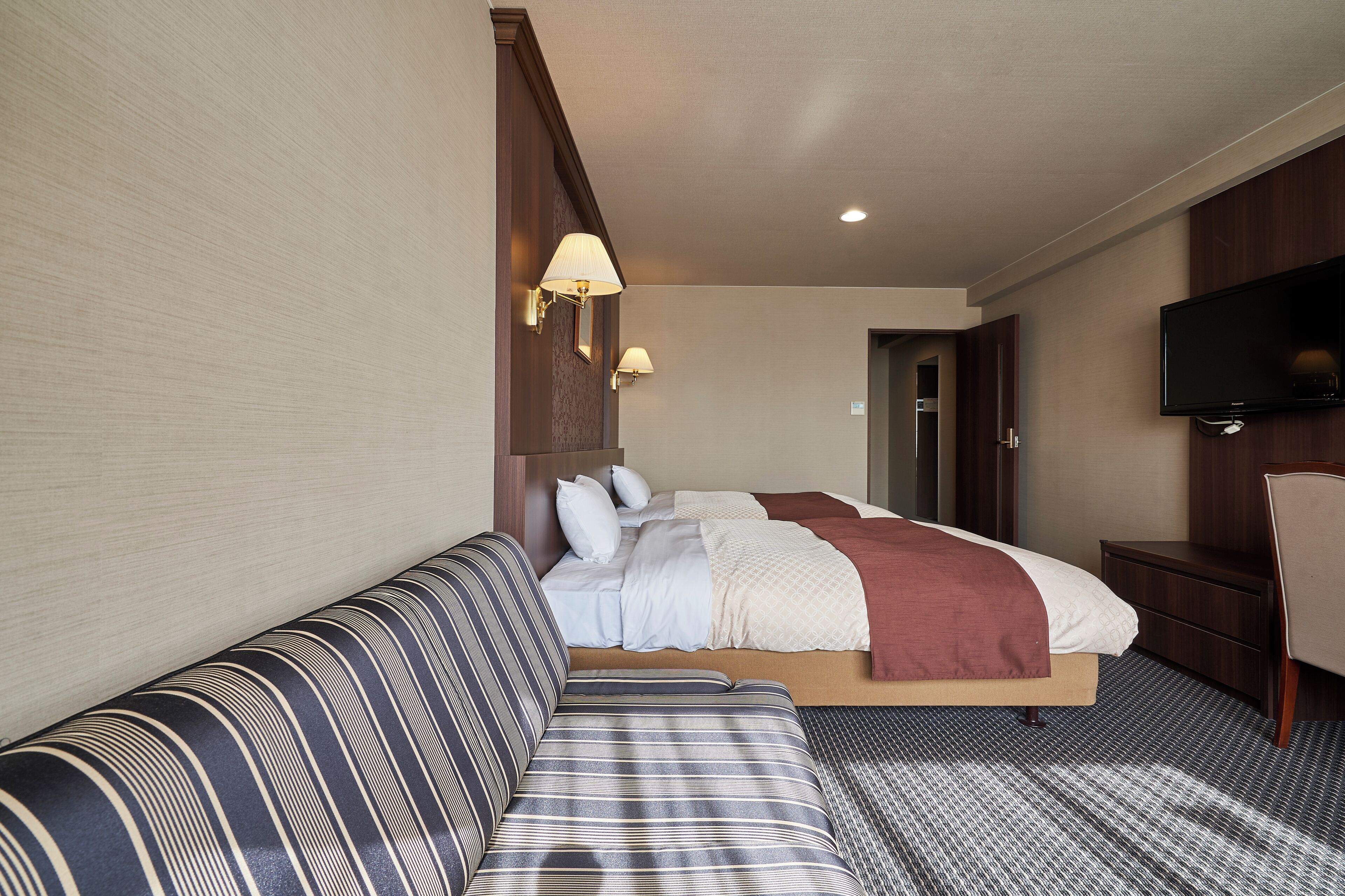 Ein Hotelzimmer mit Bett, Sofa, Fernseher und Schreibtisch.