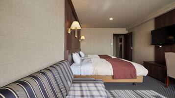 Una habitación de hotel con cama, sofá, televisor y escritorio.