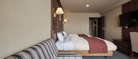 A hotel room with a bed, a sofa, a TV, and a desk.
