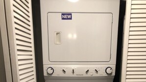 Ein kleiner, weißer Waschraum mit einem 'NEU'-Schild, einer Waschmaschine mit Frontlader und einem Trockner.